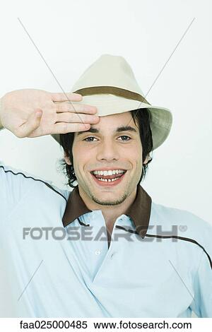 Young man wearing hat, saluting, smiling at camera View Large Photo Image Stock Photography - Young man wearing hat, saluting, smiling at camera. Fotosearch