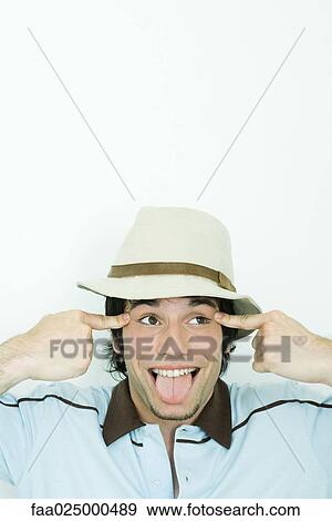 Young man wearing hat, sticking out tongue, pulling eyes to the side View Large Photo Image Stock Photo - Young man wearing hat, sticking out tongue, pulling eyes to the side. Fotosearch