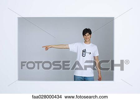 Young man wearing tee-shirt with cell phone graphic, pointing away, smiling at camera View Large Photo Image Picture - Young man wearing tee-shirt with cell phone graphic, pointing away, smiling at camera. Fotosearch
