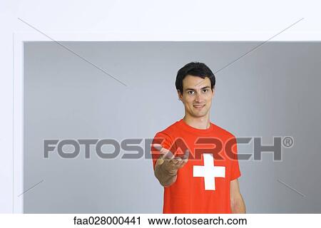 Young man wearing tee-shirt with plus symbol, holding out hand, smiling at camera View Large Photo Image Stock Image - Young man wearing tee-shirt with plus symbol, holding out hand, smiling at camera. Fotosearch