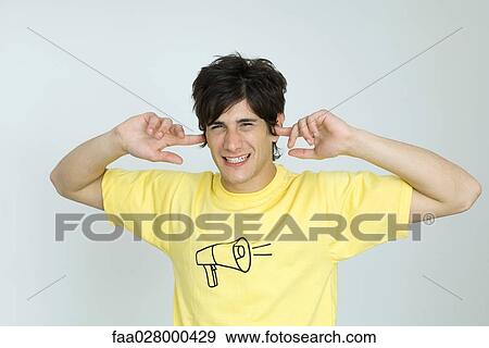 Young man wearing tee-shirt with megaphone graphic, covering ears, looking at camera View Large Photo Image Stock Photo - Young man wearing tee-shirt with megaphone graphic, covering ears, looking at camera. Fotosearch