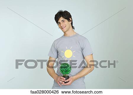 Young man wearing tee-shirt with sun graphic, holding potted plant, smiling at camera View Large Photo Image Stock Photograph - Young man wearing tee-shirt with sun graphic, holding potted plant, smiling at camera. Fotosearch