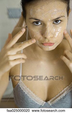 Young woman applying facial mask, looking at camera, close-up View Large Photo Image Stock Image - Young woman applying facial mask, looking at camera, close-up. Fotosearch