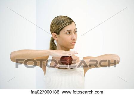 Young woman holding apple, arms raised, looking away View Large Photo Image Stock Photograph - Young woman holding apple, arms raised, looking away. Fotosearch