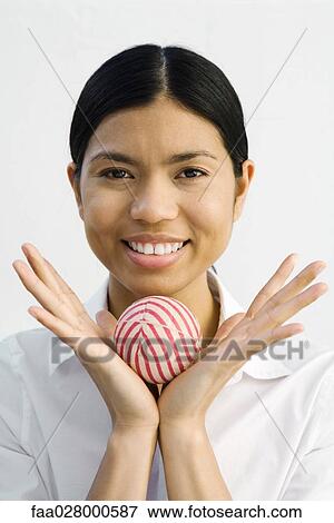Stock Photo - Young woman holding ball in hands, smiling at camera, portrait. Fotosearch