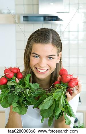 Stock Photo - Young woman holding bunches of radishes in hands, smiling at camera, portrait. Fotosearch