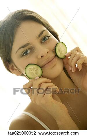 Young woman holding cucumber slices against face, smiling at camera View Large Photo Image Stock Image - Young woman holding cucumber slices against face, smiling at camera. Fotosearch