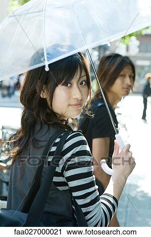 Young woman holding parasol, smiling over shoulder at camera View Large Photo Image Stock Image - Young woman holding parasol, smiling over shoulder at camera. Fotosearch