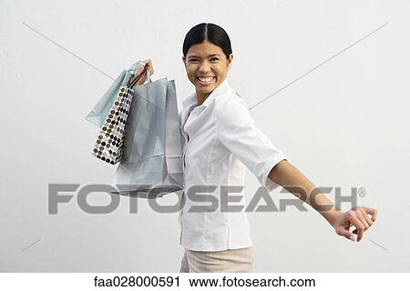 Young woman holding shopping bags, smiling at camera View Large Photo Image Stock Image - Young woman holding shopping bags, smiling at camera. Fotosearch
