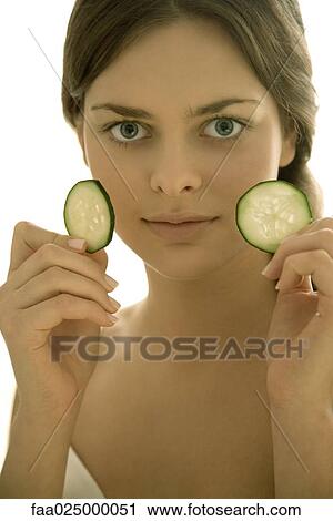 Young woman holding up cucumber slices, looking at camera View Large Photo Image Stock Image - Young woman holding up cucumber slices, looking at camera. Fotosearch