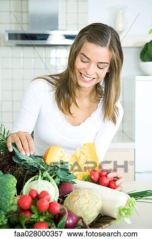 Young woman in kitchen, looking down at assorted fresh vegetables, smiling View Large Photo Image Stock Photo - Young woman in kitchen, looking down at assorted fresh vegetables, smiling. Fotosearch