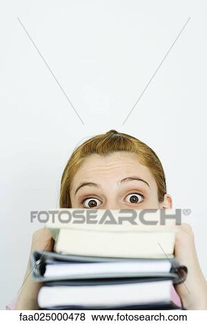 Young woman looking at camera over stack of books with wide eyes View Large Photo Image Stock Photo - Young woman looking at camera over stack of books with wide eyes. Fotosearch