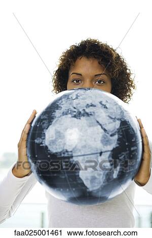 Stock Image - Young woman looking over globe at camera. Fotosearch