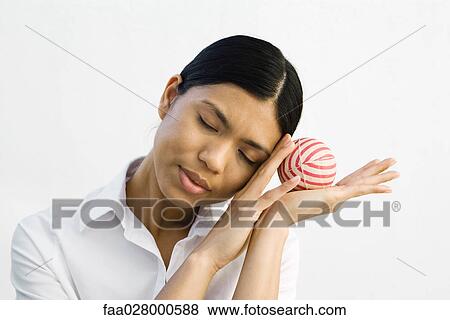 Stock Photo - Young woman resting head on hands, holding ball, eyes closed. Fotosearch
