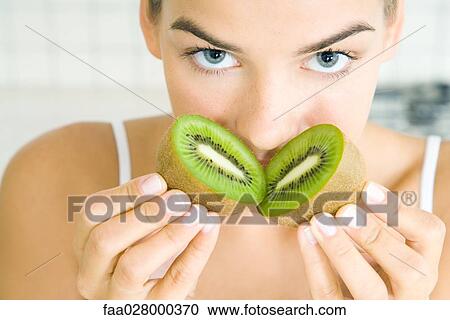 Young woman smelling freshly cut kiwi, looking at camera, close-up View Large Photo Image Stock Image - Young woman smelling freshly cut kiwi, looking at camera, close-up. Fotosearch