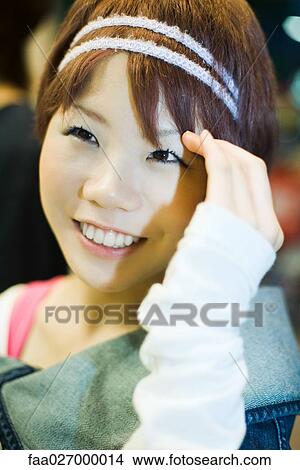 Picture - Young woman smiling, touching head, close-up. Fotosearch