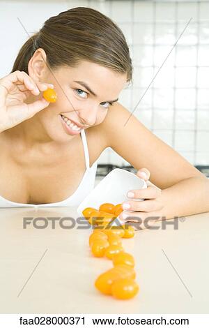 Stock Image - Young woman spilling dish of cherry tomatoes, smiling at camera. Fotosearch