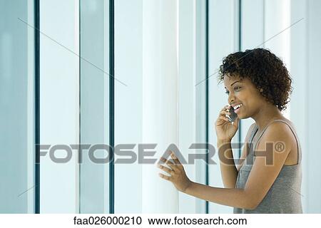 Young woman using cell phone, hand touching pole, smiling View Large Photo Image Stock Image - Young woman using cell phone, hand touching pole, smiling. Fotosearch