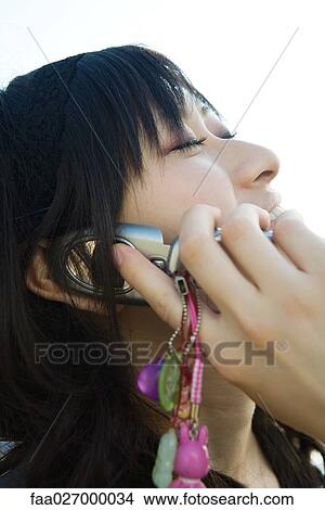 Young woman using cell phone, head back, eyes closed, close-up View Large Photo Image Picture - Young woman using cell phone, head back, eyes closed, close-up. Fotosearch