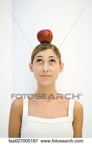 Stock Photo - Young woman with apple balanced on her head, looking up, portrait. Fotosearch