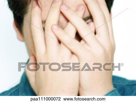 Stock Image - Teenage boy with hands covering face, close-up. Fotosearch