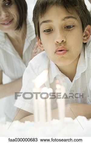 Stock Image - Boy blowing out candles on birthday cake, close-up. Fotosearch
