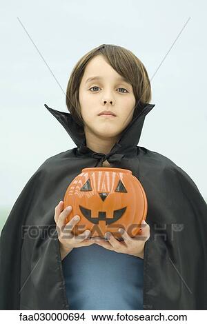 Picture - Boy dressed in vampire costume, holding jack o'lantern, portrait. Fotosearch