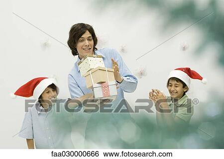 Boy knocking over stack of Christmas gifts in his older brother's arms, smiling View Large Photo Image Stock Photograph - Boy knocking over stack of Christmas gifts in his older brother's arms, smiling. Fotosearch