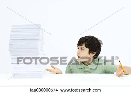Boy looking at tall stack of paper, shrugging in disbelief, holding pencil View Large Photo Image Picture - Boy looking at tall stack of paper, shrugging in disbelief, holding pencil. Fotosearch