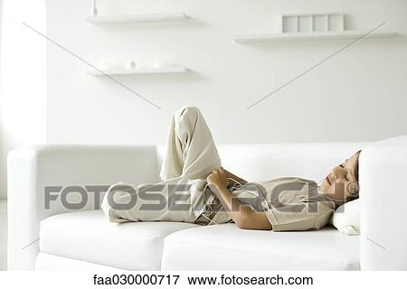 Stock Photo - Boy lying on sofa, listening to headphones, eyes closed. Fotosearch