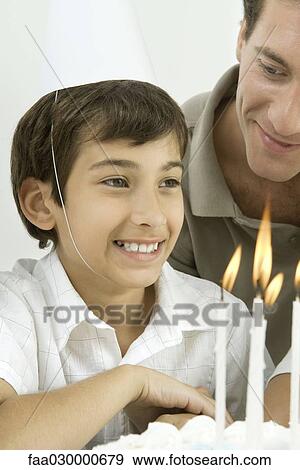 Boy next to birthday cake with lit candles, wearing party hat, smiling View Large Photo Image Stock Photo - Boy next to birthday cake with lit candles, wearing party hat, smiling. Fotosearch