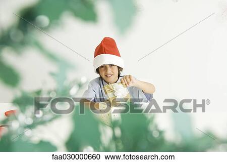 Boy opening Christmas gift, wearing Santa hat, smiling at camera View Large Photo Image Stock Image - Boy opening Christmas gift, wearing Santa hat, smiling at camera. Fotosearch
