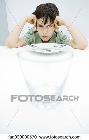 Boy sulking at kitchen table, leaning on elbows, empty glass in foreground View Large Photo Image Stock Image - Boy sulking at kitchen table, leaning on elbows, empty glass in foreground. Fotosearch
