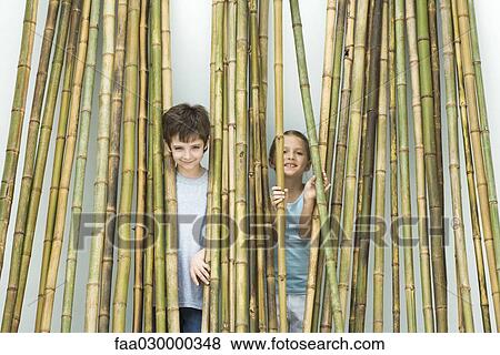 Stock Photo - Brother and sister standing behind bamboo, smiling at camera. Fotosearch