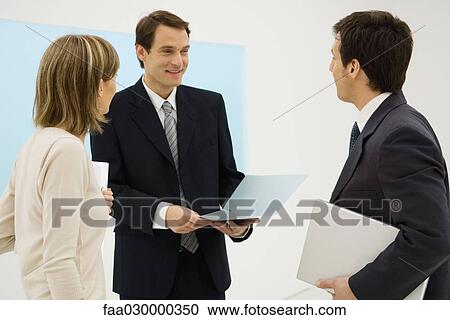 Business associates standing together, discussing, one holding folder View Large Photo Image Stock Image - Business associates standing together, discussing, one holding folder. Fotosearch
