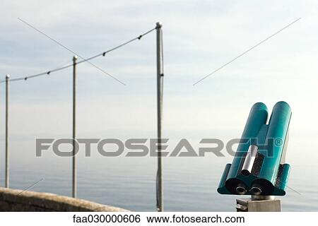 Coin-operated binoculars at the water's edge, poles with lights in background View Large Photo Image Stock Photograph - Coin-operated binoculars at the water's edge, poles with lights in background. Fotosearch