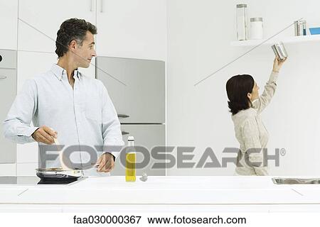 Couple in kitchen, man cooking at stove, looking over shoulder, wife reaching for cannister View Large Photo Image Stock Photo - Couple in kitchen, man cooking at stove, looking over shoulder, wife reaching for cannister. Fotosearch