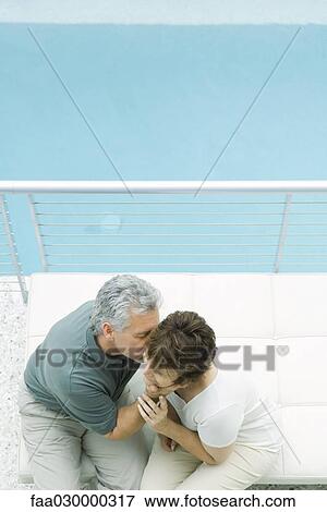 Stock Photo - Couple sitting on balcony, man kissing woman's cheek, high angle view. Fotosearch
