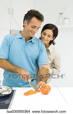 Couple standing together in kitchen, man slicing tomato, both smiling View Large Photo Image Picture - Couple standing together in kitchen, man slicing tomato, both smiling. Fotosearch