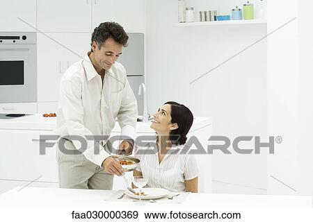 Couple together at kitchen table, man serving woman's dinner, both smiling View Large Photo Image Stock Photo - Couple together at kitchen table, man serving woman's dinner, both smiling. Fotosearch