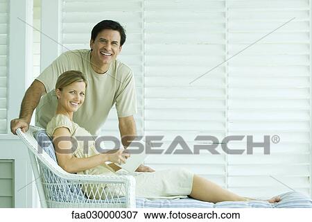Couple together on patio, smiling at camera, woman holding book View Large Photo Image Stock Photo - Couple together on patio, smiling at camera, woman holding book. Fotosearch