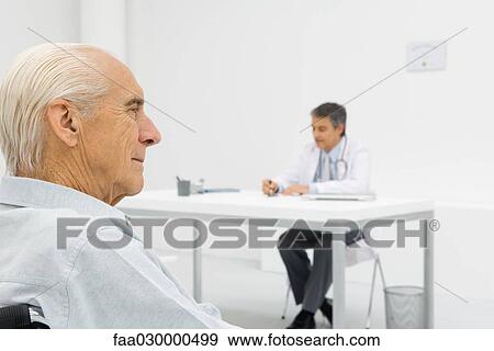 Stock Photo - Doctor working at desk, focus on senior patient in foreground. Fotosearch