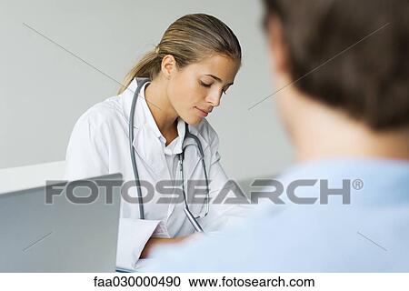 Doctor writing at desk, patient in foreground View Large Photo Image Stock Image - Doctor writing at desk, patient in foreground. Fotosearch