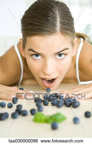 Fresh blueberries scattered across counter, young woman opening mouth to eat one View Large Photo Image Stock Photograph - Fresh blueberries scattered across counter, young woman opening mouth to eat one. Fotosearch
