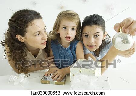 Girl beside mother and sister, holding up Christmas ornament, smiling at camera View Large Photo Image Stock Image - Girl beside mother and sister, holding up Christmas ornament, smiling at camera. Fotosearch