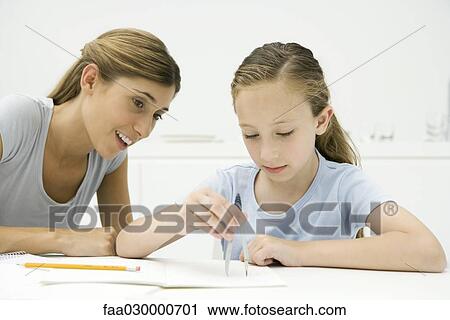 Stock Image - Girl doing homework, using drawing compass, mother watching. Fotosearch