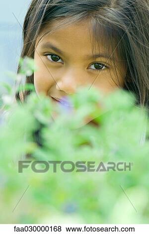 Girl smiling at camera, looking over plant in blurred foreground View Large Photo Image Stock Photo - Girl smiling at camera, looking over plant in blurred foreground. Fotosearch