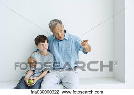 Grandfather and grandson sitting together, man pointing, boy holding apple View Large Photo Image Stock Image - Grandfather and grandson sitting together, man pointing, boy holding apple. Fotosearch