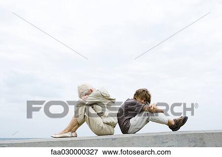 Grandmother and grandson sitting back to back, heads down, arms folded, boy looking at camera View Large Photo Image Stock Photo - Grandmother and grandson sitting back to back, heads down, arms folded, boy looking at camera. Fotosearch