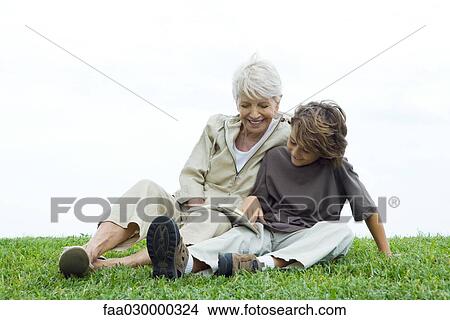 Grandmother and grandson sitting together outdoors, reading book View Large Photo Image Picture - Grandmother and grandson sitting together outdoors, reading book. Fotosearch